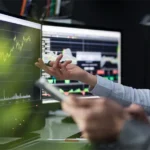 Zwei Personen analysieren Daten auf Monitoren mit steigenden Kurven, um die PSS-Definition (Product-Service-System) zu überprüfen und passende Use Cases & Szenarien zu entwickeln. Diese Phase hilft dabei, spezifische Anwendungsfälle zu identifizieren und das System effektiv zu planen. Two people analyze data on monitors with rising curves to review the PSS definition (Product-Service-System) and develop relevant use cases & scenarios. This phase helps identify specific applications and effectively plan the system.