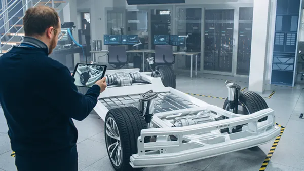 An engineer uses a tablet to analyze a vehicle chassis in a lab. The image illustrates modern mobility concepts.