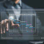 Eine Person in einem Anzug arbeitet mit einem digitalen Gantt-Diagramm, das auf einem transparenten Bildschirm angezeigt wird. Der Zeitplan zeigt verschiedene Phasen der PSS-Planung mit Aufgaben, Meilensteinen und Projektschritten. A person in a suit interacts with a digital Gantt chart displayed on a transparent screen. The schedule outlines various phases of PSS planning, including tasks, milestones, and project steps.