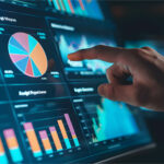 Eine Hand zeigt auf einen Bildschirm, der verschiedene Diagramme und Grafiken darstellt, darunter Kreis- und Balkendiagramme. In diesem Moment wird der Prozess des Value Engineering & Analysis visualisiert, um Kosten und Nutzen von Komponenten oder Systemen zu bewerten und Optimierungspotenziale zu identifizieren. A hand points to a screen displaying various charts and graphs, including pie and bar charts. This represents the process of Value Engineering & Analysis, aimed at evaluating the costs and benefits of components or systems and identifying opportunities for optimization.