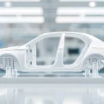 Seitenansicht einer Auto-Karosseriestruktur in einem modernen Werk, montiert auf einer Plattform, die präzise Fertigungstechnologien symbolisiert. Das Bild verdeutlicht den Einsatz von Giga Casting für die Herstellung großer und komplexer Fahrzeugkomponenten. Side view of a car body structure in a modern plant, mounted on a platform symbolizing precision manufacturing technologies. The picture illustrates the use of Giga Casting for the production of large and complex vehicle components.